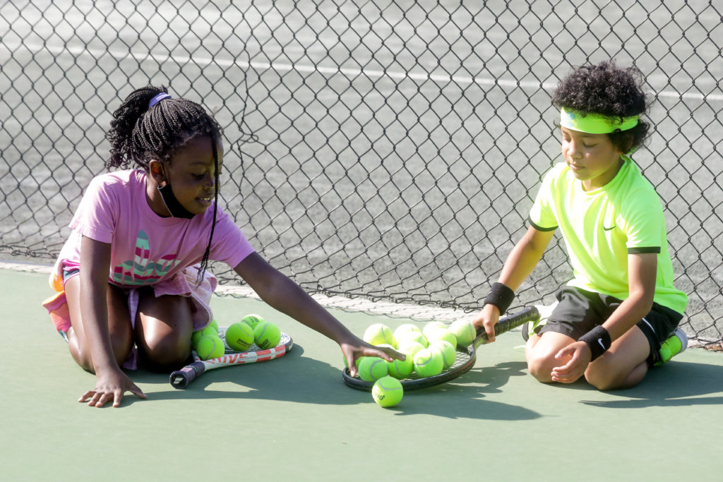 2 kids playing with tennis balls on a tennis court